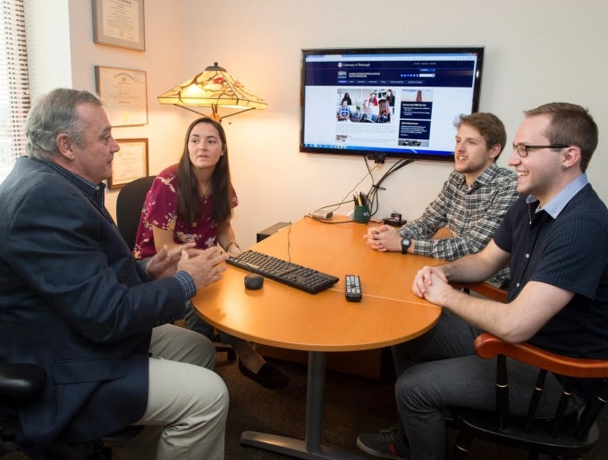 picture of teacher and students around a table with computer and display 